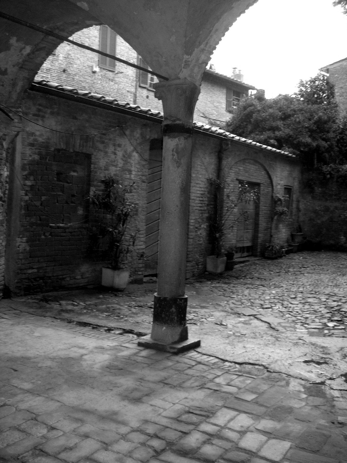 The portico on the courtyard before the works, with the old column that was later replaced and the wet cobbles