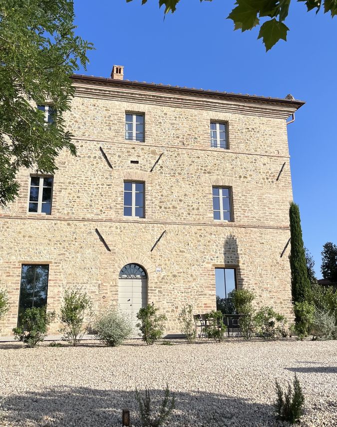 Façade of the farmhouse with the windows and the arched portal, and the gravel path