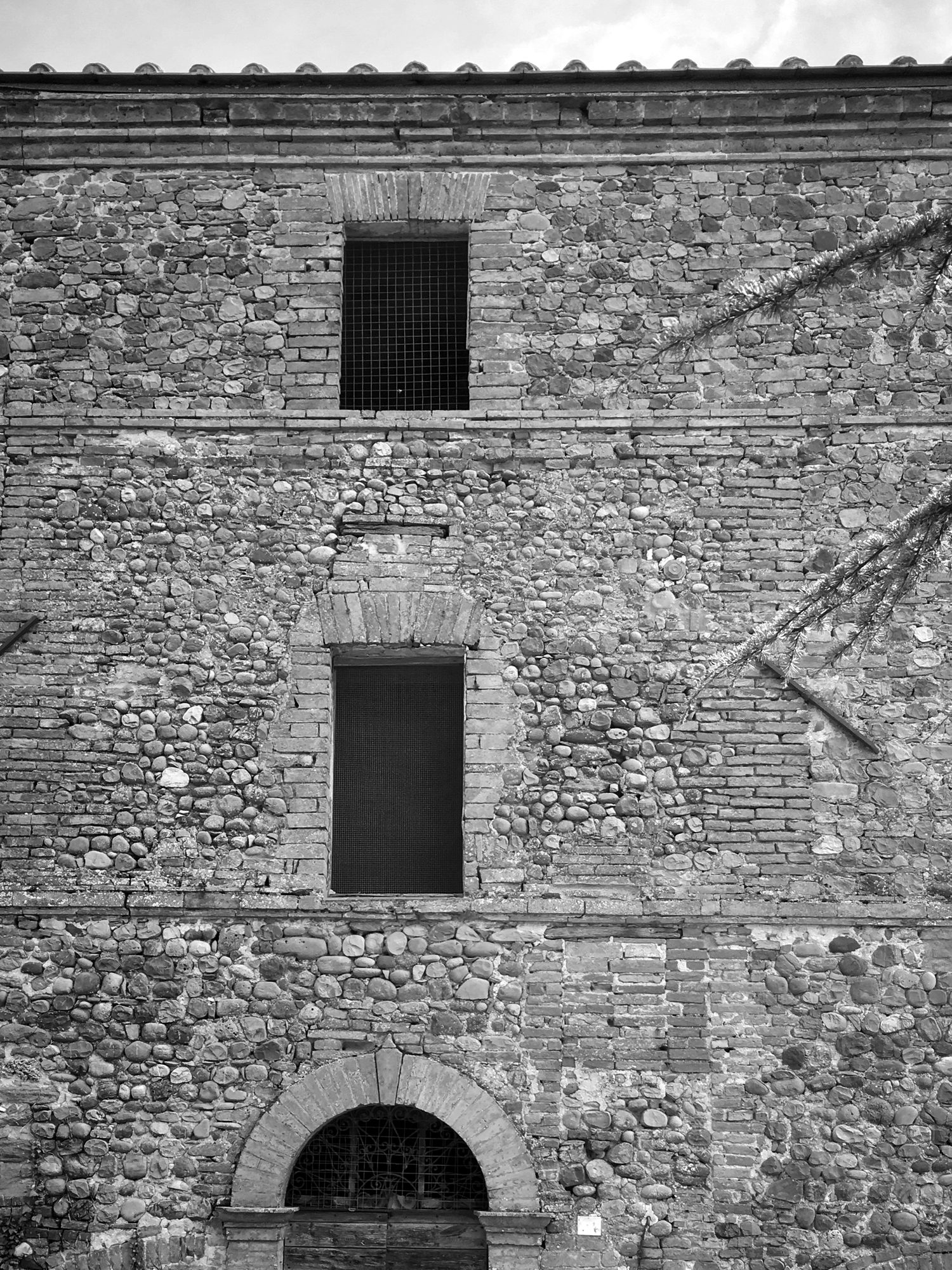 The same façade in 2018, with the windows closed by grilles, the damaged masonry and the wooden door