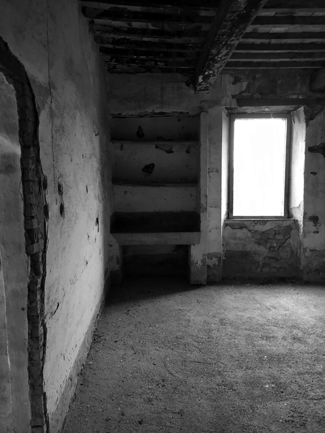 Interior room with peeling plaster and a window with no frame