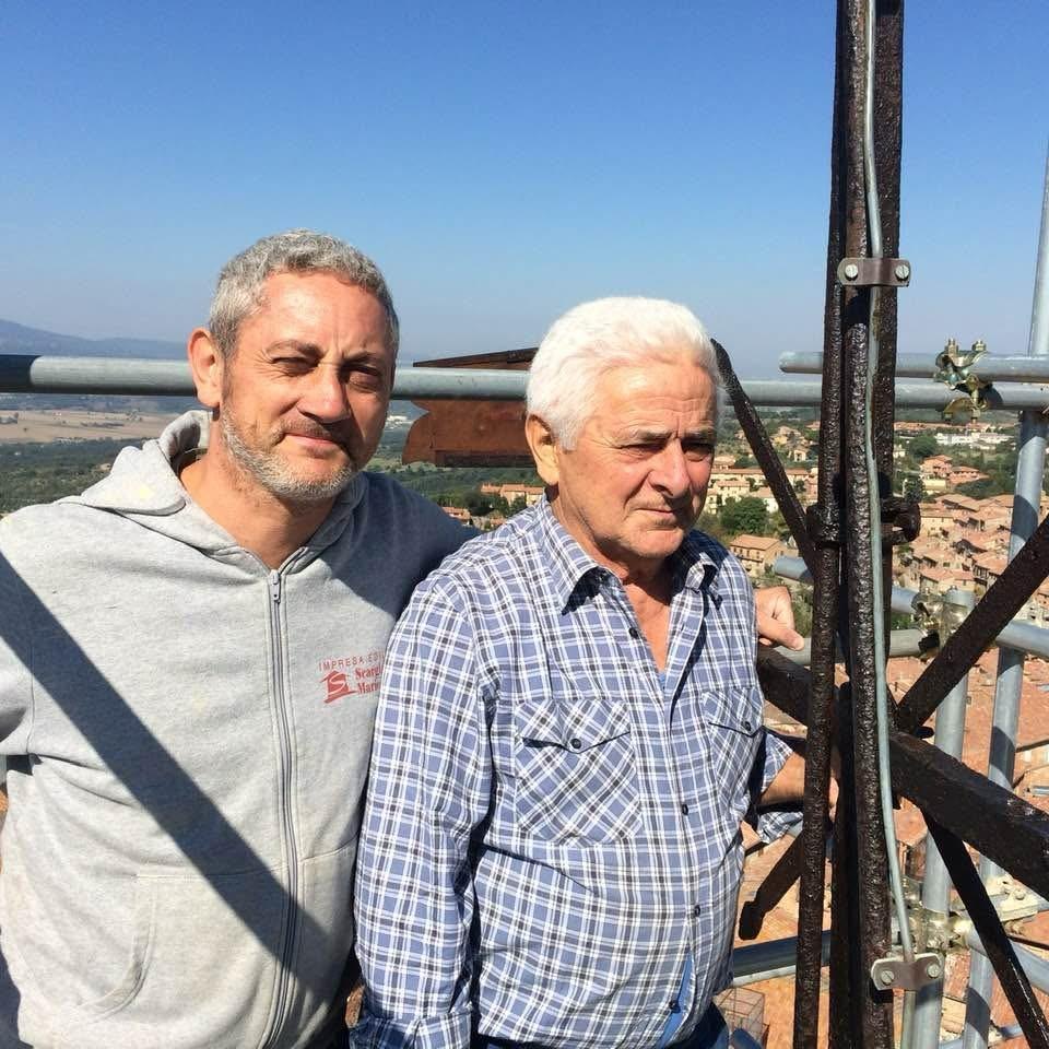 Mario Scargiali with his father Aldo at the top of the Cathedral bell tower in Città della Pieve, on the scaffolding, with the town roofs below