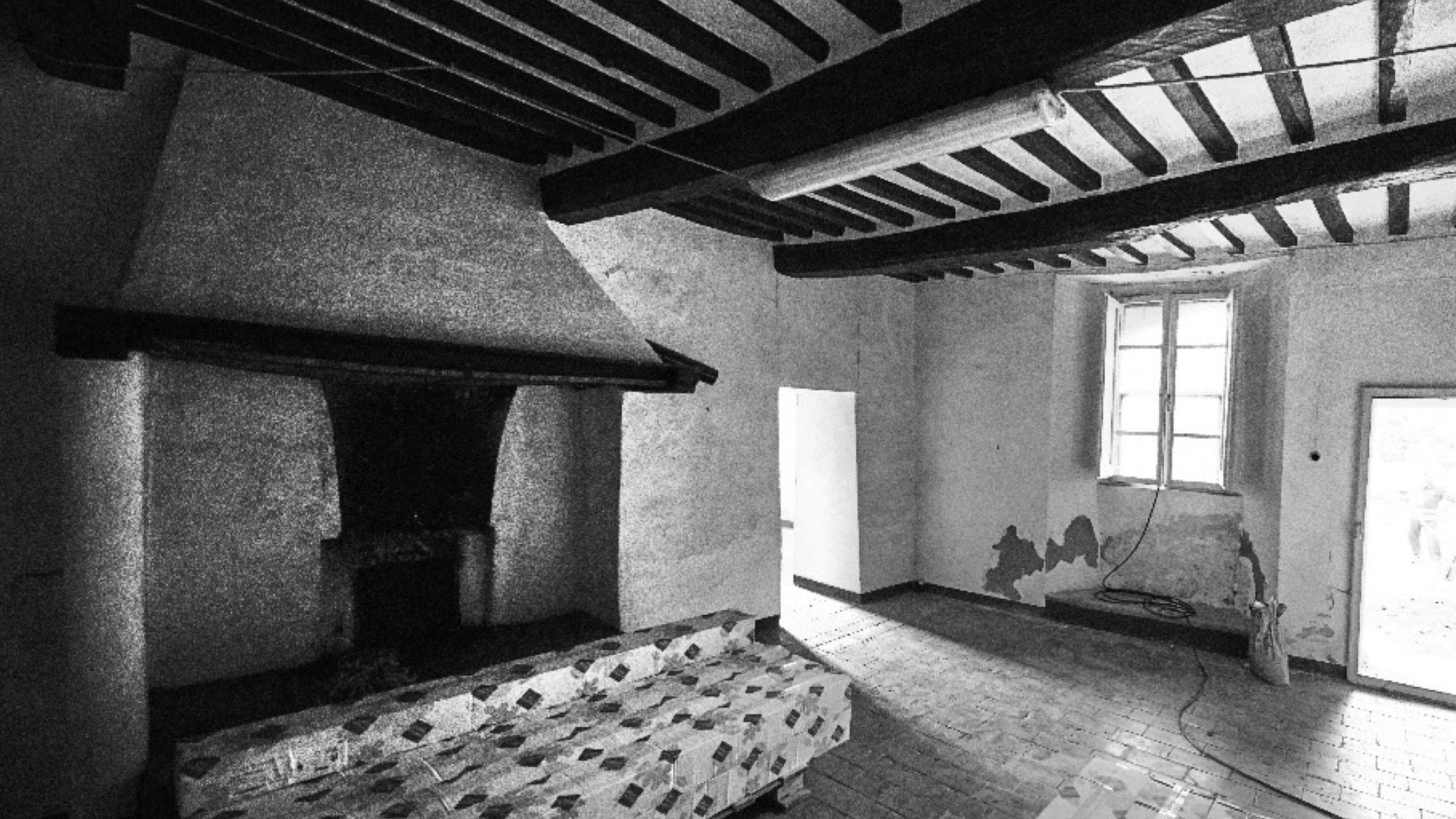 La stessa stanza prima del restauro: pavimento in graniglia, intonaci rovinati e un materasso a terra