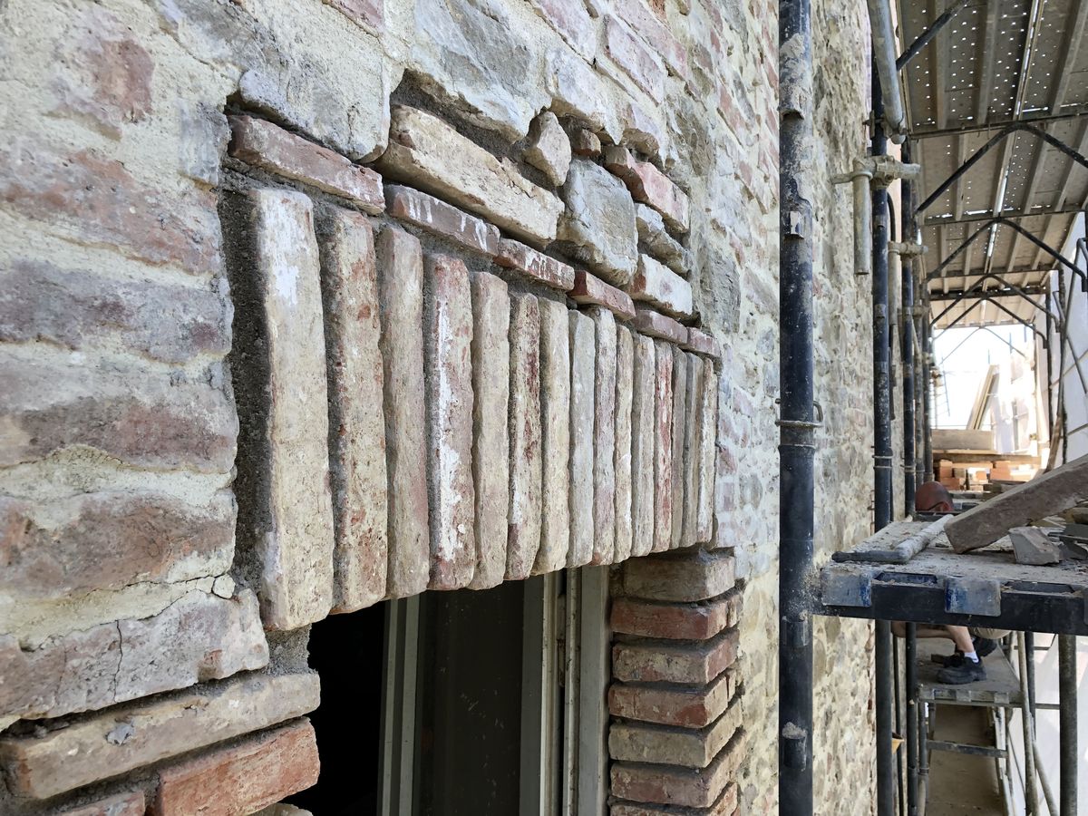Architrave in mattoni sopra una finestra della facciata, con il ponteggio