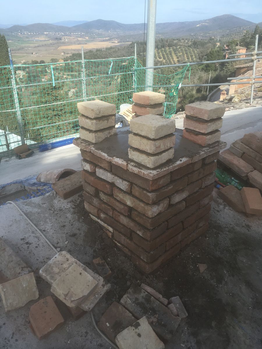 Comignolo in mattoni in costruzione sul tetto, con le colline sullo sfondo