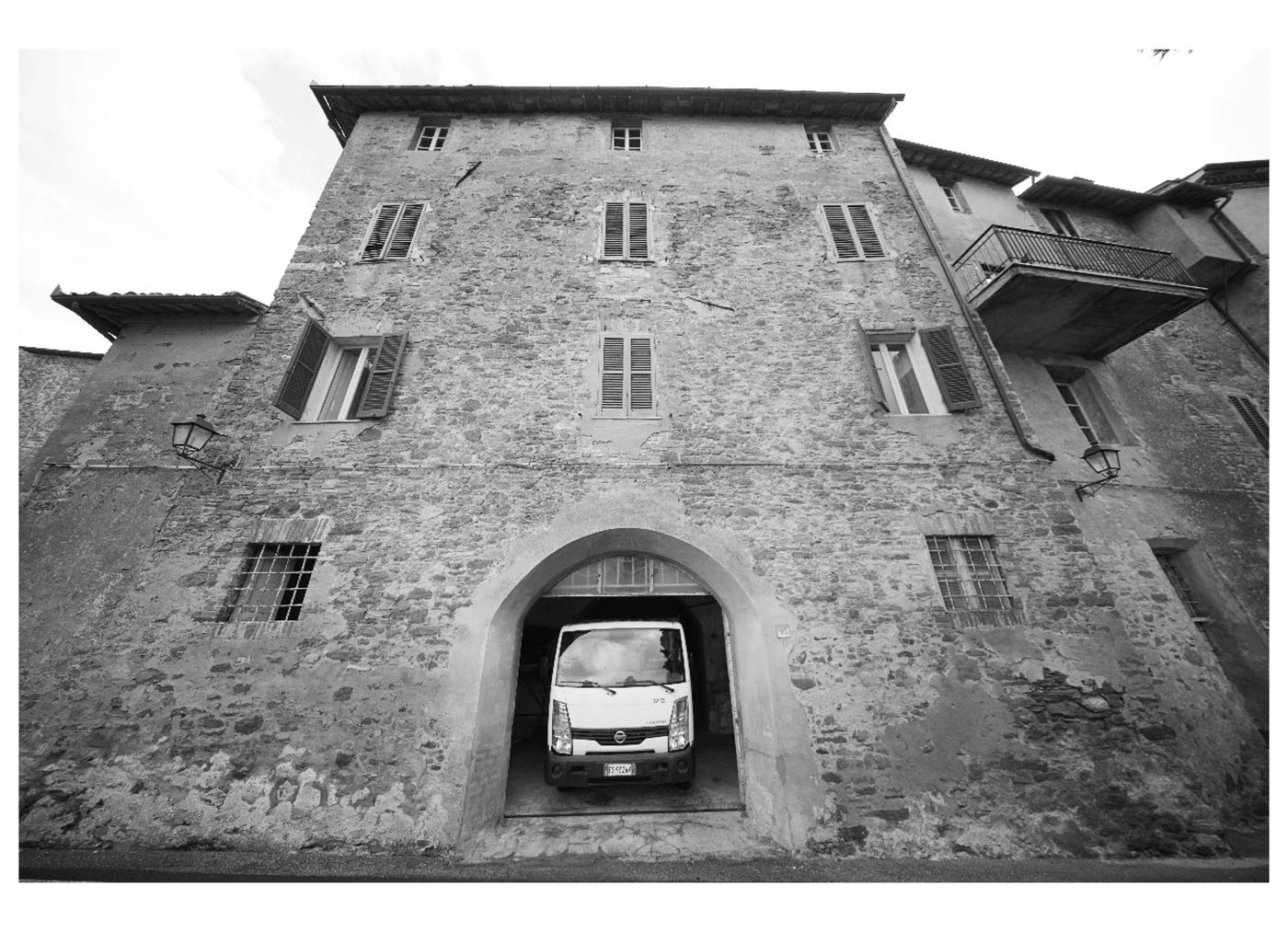Facciata in pietra del palazzo prima del restauro, con il portone ad arco aperto su un furgone