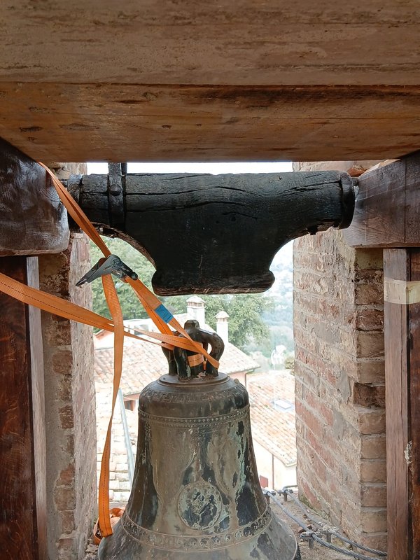 A decorated bronze bell, secured with orange straps beneath the wooden headstock