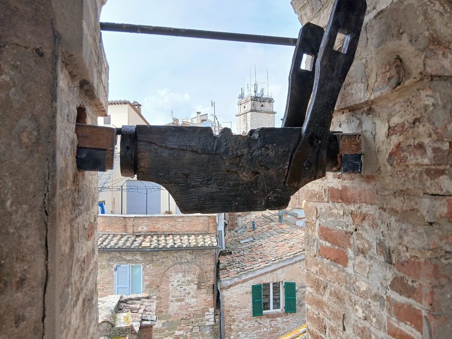 The wooden headstock of a bell, with the roofs and towers of Perugia in the background