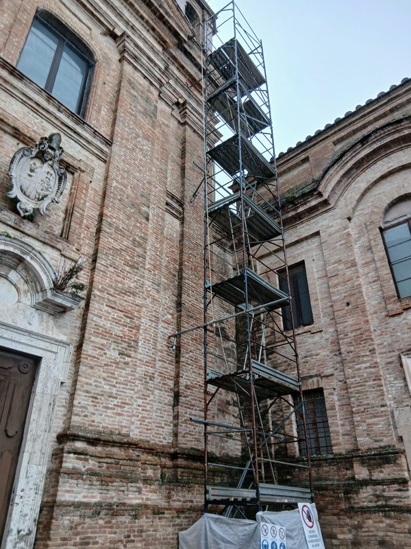 The scaffolding tower along the brick façade, next to the stone coat of arms of the church