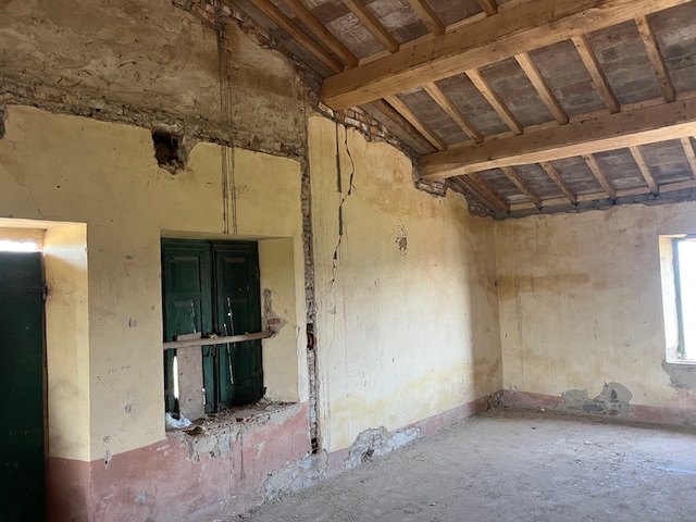 A first-floor room with a timber-beam ceiling and cracks in the walls