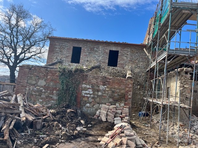 A stone and brick outbuilding, with building materials in front and the scaffolding