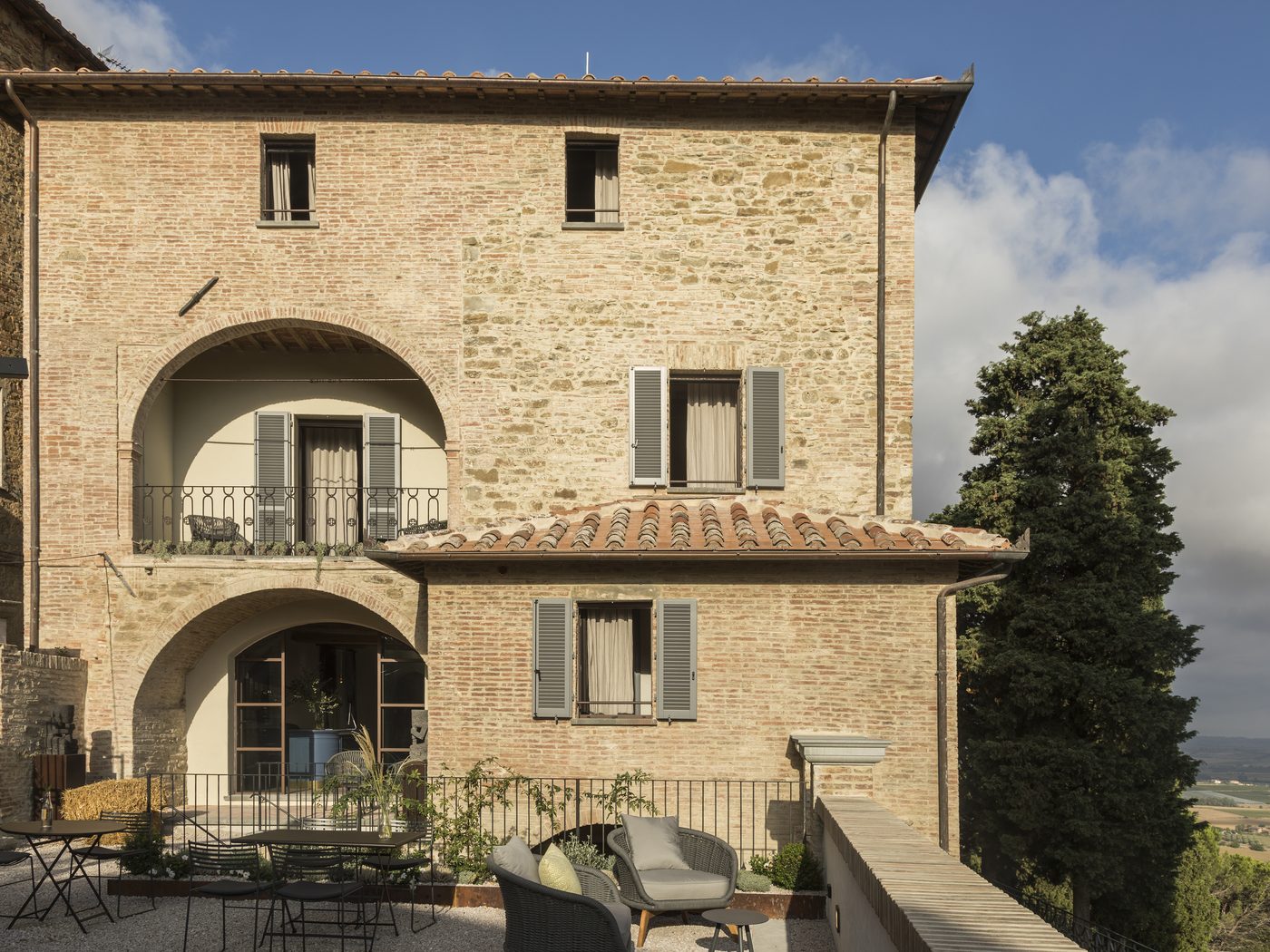 Stone and brick façade of Il Rastrello with the arched loggia and the terrace