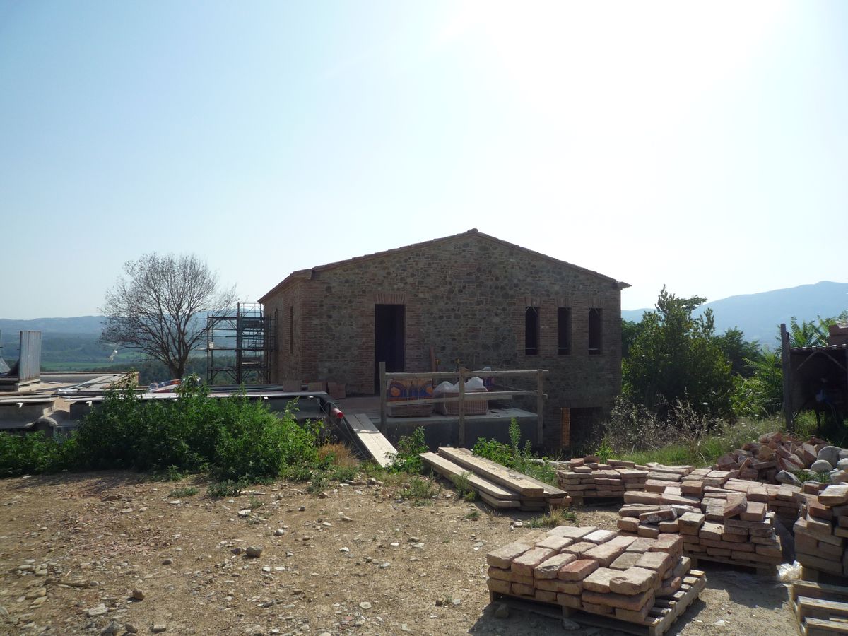 Il casolare in pietra e i bancali di mattoni pronti per la posa