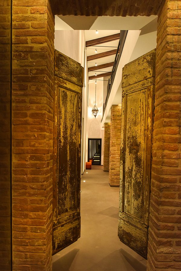 Due portoni antichi in legno tra i pilastri in mattoni, con il corridoio illuminato dietro